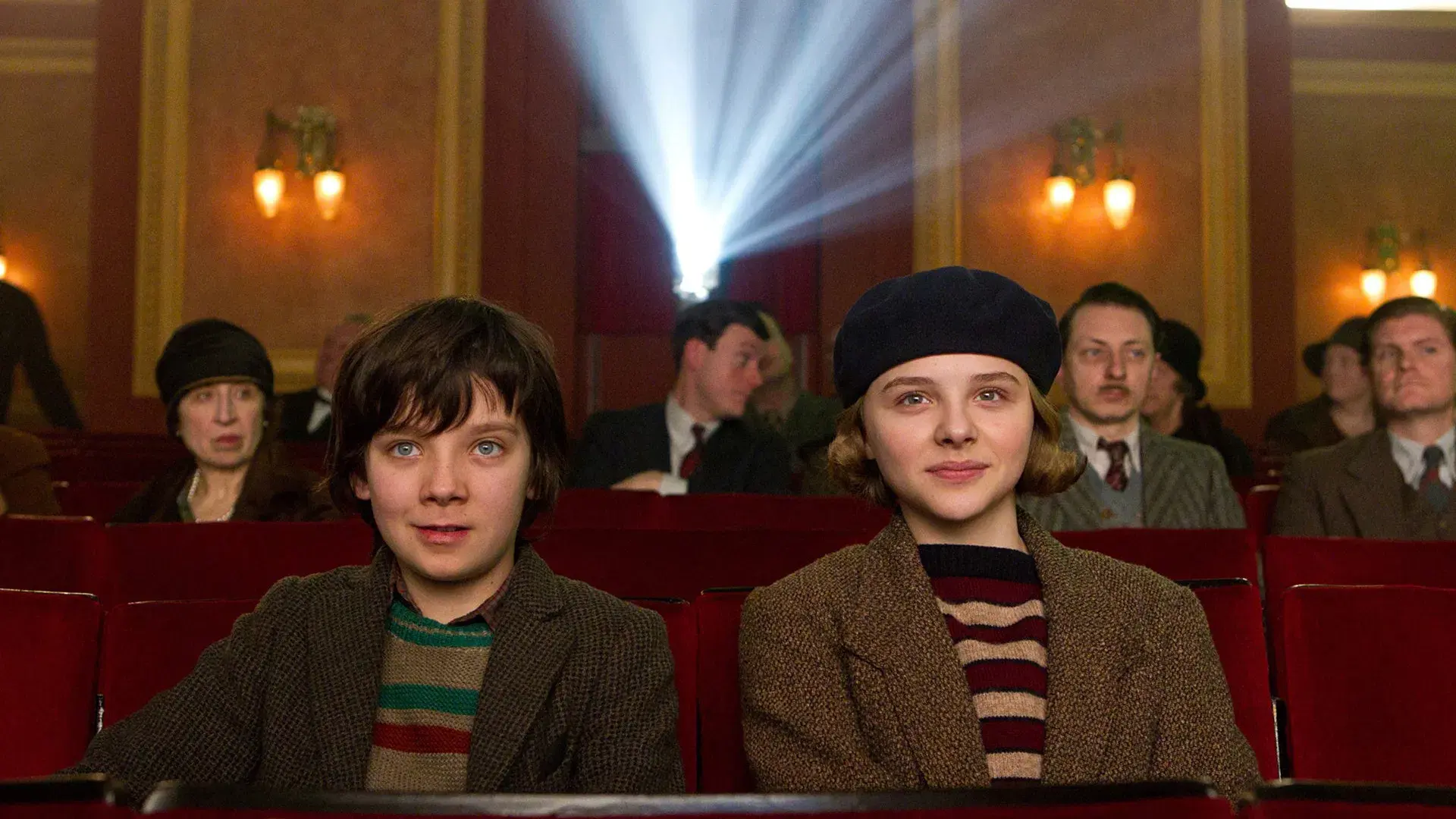 Hugo and Isabelle sitting in a movie theater with a projector behind them